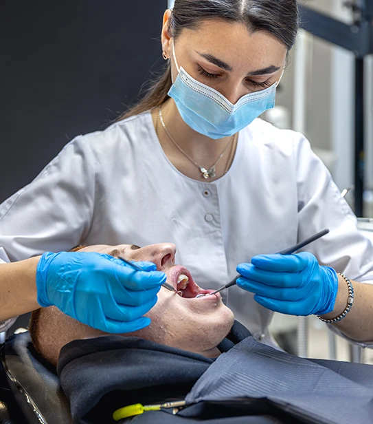 A professional female dentist wearing a mask and blue gloves using a dental mirror and probe to examine a patient's teeth.