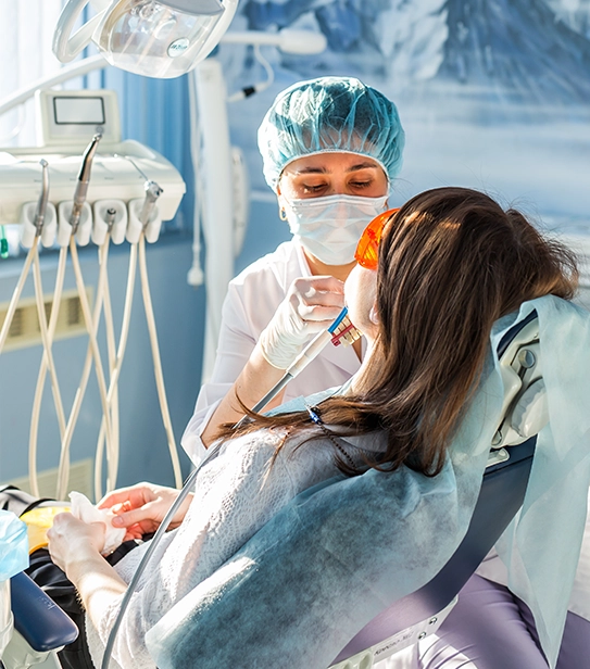 A close-up of a dental model held by gloved hands showing a titanium implant screw integrated into the jawbone between two healthy natural teeth.